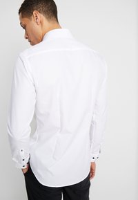 Witte lange mouwen shirt, gladde stof, gestructureerde kraag, gebogen zoom, zwarte knoopaccenten op de mouwen, met een strak, passend ontwerp.