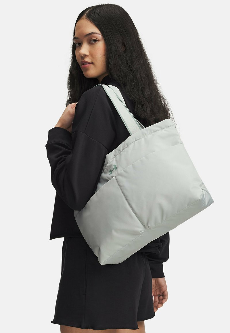 Bolso tote acolchado gris claro con una textura suave, que cuenta con dos asas y un logo sutil en el lateral. Forma rectangular minimalista.