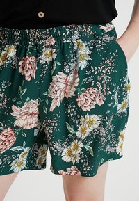 Blommiga shorts med resårmidja, tillverkade av grönt tyg med rosa och vita blommor, samt små bladdetaljer och sidofickor.