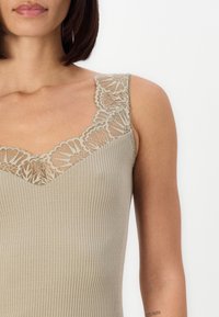 Beige ribbattuori tank top, jossa on pitsikoristeet kaula-aukossa ja olkaimissa. Pehmeä materiaalitunti, vartalonmyötäinen malli ja V-muotoinen etuosa.