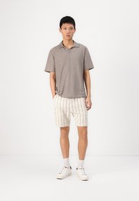 Polo de manga curta às riscas cinzentas, combinado com calções creme com riscas verticais pretas. O modelo usa ténis brancos com meias cinzentas.