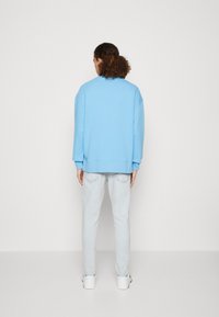 Sudadera azul clara con hombros caídos, puños y dobladillo acanalados, combinada con jeans de mezclilla claros y zapatillas blancas. Textura suave.