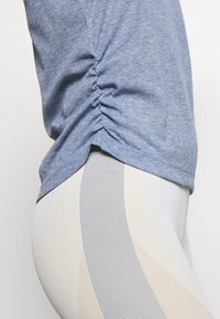 T-shirt azzurro chiaro a costine con arricciature laterali, abbinato a leggings a righe crema e azzurro chiaro. Tessuto testurizzato con un design aderente.