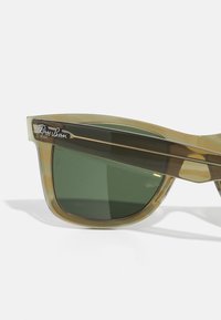 Ray-Ban aurinkolasit, joissa on läpikuultava oliivinvihreä kehys ja tummanvihreät linssit, joissa on tyylikkäät linjat ja rohkeat templeet.