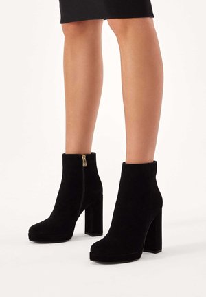 Black suede ankle boots with a chunky block heel and side zipper, featuring a rounded toe and a smooth texture.