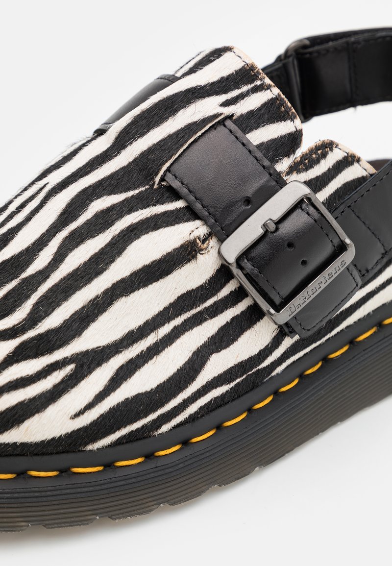 Zebramuster-Sandalen mit einer schwarzen Leder-Schnalle, strukturiertem Obermaterial und einer dicken Gummisohle mit gelben Nähten.