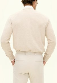 Beiger Strickpullover mit rundem Halsauschnitt, strukturiertem Stoff und langen Ärmeln, kombiniert mit hellen, taillierten Hosen mit Gesäßtaschen.