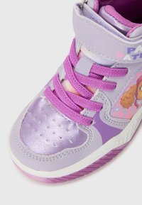 Zapatilla alta morada con material sintético brillante, acentos texturizados y cordones rosas. Presenta un gráfico de personaje en el costado.