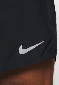 Mustat urheilushortsit, jotka on valmistettu sileästä kankaasta ja joissa on suuri, heijastava Nike-tunnuslogo alaosassa.