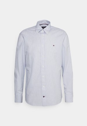 Chemise à manches longues, bleu clair et blanc à fines rayures, boutonnée, col boutonné et petit logo brodé rouge, blanc et bleu sur la poitrine.