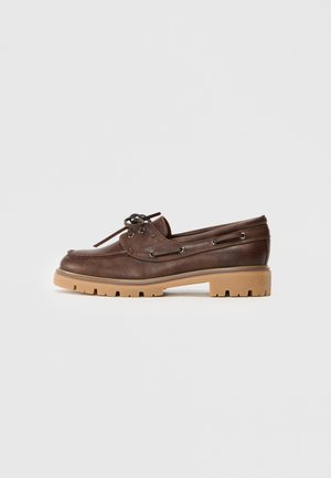 Brązowe skórzane buty żeglarskie z okrągłym noskiem, detalami w postaci sznurowadeł oraz kontrastową, tanową gumową podeszwą z teksturowanym wzorem bieżnika.