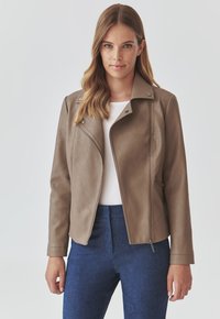 Brown faux leather jacket with a fitted design, asymmetrical front zipper, and snap fasteners. Paired with a white top and blue trousers.