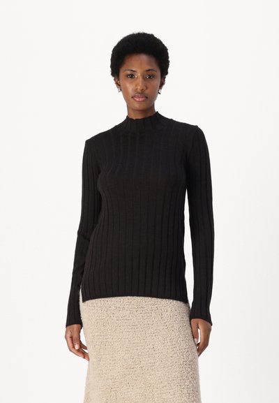 Zwarte ribbel turtleneck trui met lange mouwen, met een getailleerde pasvorm en zachte textuur. Draagt bij een lichtgekleurde, gestructureerde rok.