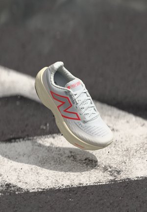 Light gray running shoe with a textured upper and a bold red logo. Features a rounded toe and cushioned cream-colored sole.