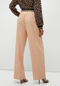 Pantaloni a palazzo plissettati color pesca con vita elastica. Il tessuto ha una texture liscia e una silhouette fluida, adatta per un look casual.