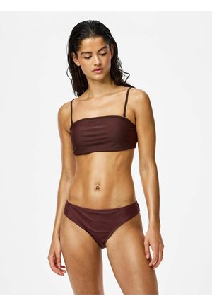 Kobieta z mokrymi włosami, ubrana w bordowy bikini bandeau na cienkich ramiączkach, stoi na jednolitym białym tle.