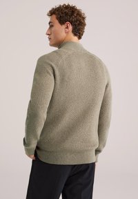 Oliwkowy sweter dzianinowy z wysokim kołnierzem, prążkową fakturą i dopasowanymi mankietami. Prezentowany z tyłu, odsłaniający teksturowany wzór materiału.