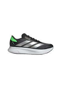 Chaussure de course noire et grise avec semelle blanche, accent vert au talon et trois rayures argentées sur le côté, vue du profil extérieur.