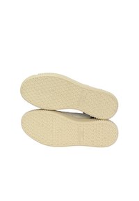 Suole di scarpe in gomma beige con motivi testurizzati, caratterizzate da un design esagonale e piccoli punti antiscivolo per una migliore aderenza. Visibile il marchio.