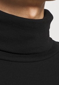 Zwarte coltrui met ribbeltextuur. Aansluitend ontwerp, gladde stof en hoge kraag zichtbaar, met schone lijnen en minimale details.