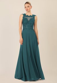 Vestido largo en color teal con un corsé ajustado que presenta encaje floral y adornos de cuentas. Falda fluida hecha de un tejido ligero, con un escote transparente.