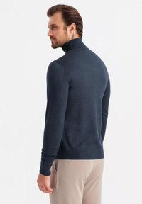 Námořnický modrý rolák s dlouhými rukávy a žebrovanými manžetami. Měkká textura, fitted design, zobrazeno zezadu. V kombinaci se světlými kalhotami.