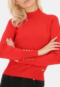 Czerwony sweter z golfem wykonany z materiału o prążkowanej strukturze. Posiada złote guziki przy mankietach oraz dopasowany krój. Miękka tekstura i jednolity kolor.