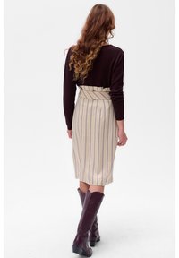Knie-lange gestreepte rok in beige en lichtblauw met een aangesloten taille, gecombineerd met een donker langemouwen top en kniehoge bordeauxrode laarzen.