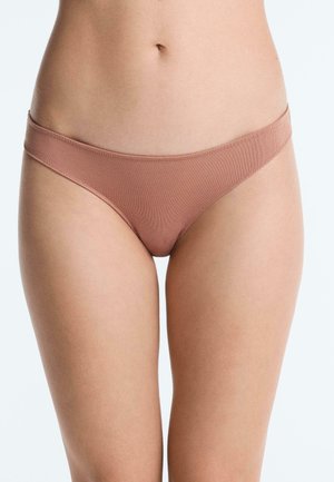 Tors feminin care poartă lenjerie de tip bikini maro deschis, cu model nervurat, pe fundal alb simplu.