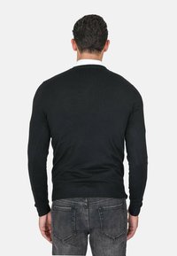 Maglione nero a maglia con colletto rotondo, maniche lunghe e vita aderente. Indossato con jeans grigi, che mostrano una sottile texture nel tessuto.