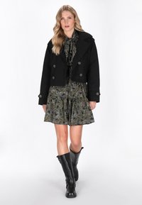 Giacca cropped nera con bottoni doppi su un vestito a fantasia floreale scura. Stivali neri al ginocchio completano il look.