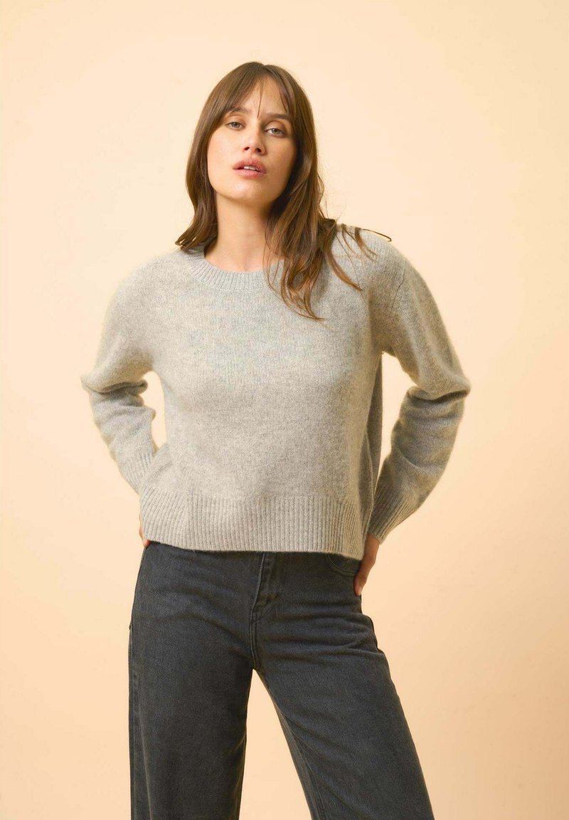 Pull en maille gris clair avec un col rond, des poignets et un ourlet côtelés, associé à un pantalon en denim foncé. Texture douce, coupe décontractée.