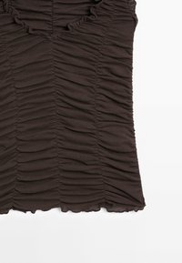 Tissu noir froncé avec des coutures verticales rassemblées et des bords à volants, probablement partie d’un vêtement ajusté comme un haut ou une robe.