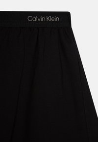 Fekete Calvin Klein sportnadrág puha anyagból. Rugalmas derékpánttal rendelkezik, amelyen logó található, valamint oldalt redőzött részletekkel.