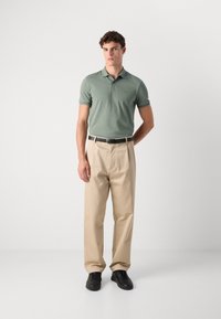 Lysegrønn polo med korte ermer, beige bukser og svarte sko. Poloen har en liten logo på brystet og en avslappet passform.