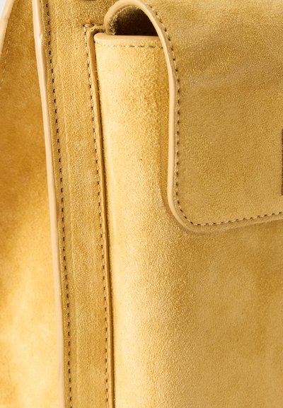 Κοντινό πλάνο μιας γωνίας μιας τσάντας από ταμπά σουέντ, που δείχνει λεπτομερή ραφή και υφή σουέντ με λείο δερμάτινο περίγραμμα.