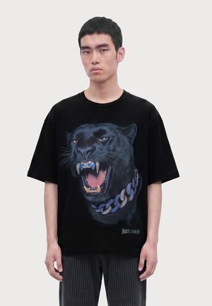 Jeune homme portant un t-shirt noir avec un grand graphisme d'une panthère noire rugissante avec un collier chaîne bleu et argenté.