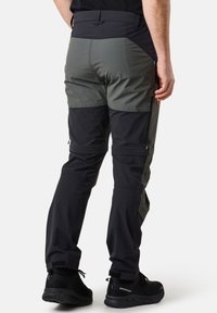 Pantalons de randonnée pour hommes avec un mélange de panneaux gris foncé et noirs, fabriqués dans un matériau léger et dotés de poches zippées, conçus pour la mobilité.
