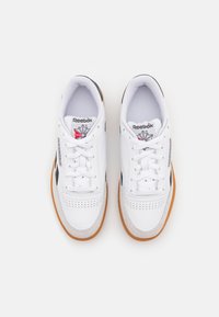 White leather sneakers with black accents, round toe, lace-up design, perforated detailing, and a gum rubber outsole. Reebok logo on the tongue.