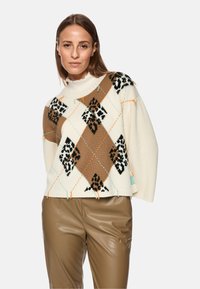 Cream knit sweater features an argyle pattern in brown, black, and orange, with relaxed fit and ribbed hem. Paired with brown faux leather pants.