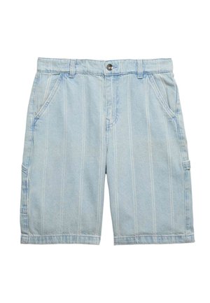 Dreng står med den ene hånd i lommen iført en løs hvid t-shirt, lyse denimshorts, hvide sokker og brune sneakers.