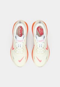 Αθλητικά παπούτσια με απαλό κρεμ επάνω μέρος, πορτοκαλί σόλες, λευκά κορδόνια και υφή σχεδίασης. Διαθέτουν κόκκινες εσωτερικές σόλες με λογότυπο.