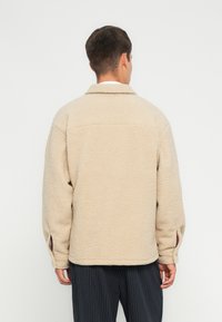 Beez fleece jakk, millel on tekstuuriga pind, kaelus ja külgmised lõhed varrukates. Tagantvaade näitab mugavat istuvust ja sirget äärt.