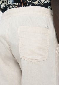 Σορτς από λινό σε ανοιχτό μπεζ χρώμα με ελαστική μέση, διαθέτουν μία τσέπη στο πίσω μέρος. Υφή υφάσματος με φυσικό φινίρισμα.