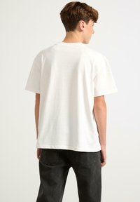 T-shirt bianco in cotone con vestibilità ampia, maniche corte e collo rotondo. Tessuto liscio e senza loghi o pattern visibili.