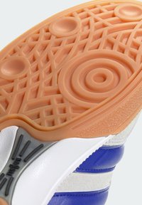 Sneaker sole with textured orange rubber featuring circular and geometric patterns; white leather and blue accents on the upper portion.