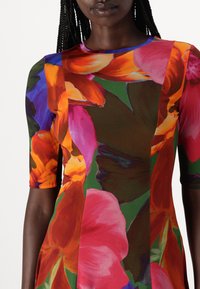 Robe à motif floral présentant des couleurs vives comme le rouge, l'orange et le vert. Fabriquée en tissu extensible avec un col rond et des manches courtes.