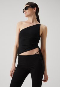 Haut noir à une épaule fabriqué en tissu lisse, avec des détails froncés et des liens latéraux ajustables. Assorti à un pantalon noir ajusté.