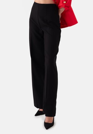 Zwarte high-waisted broeken met een op maat gemaakte pasvorm, voorzien van voorplooien en een lichte textuur. Gecombineerd met puntige zwarte hakken.