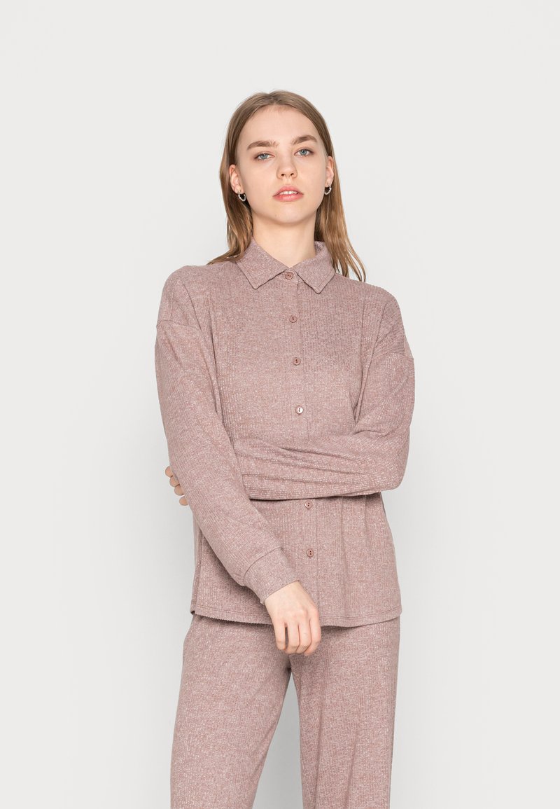 Camisola malha rosa claro com fecho frontal por botão, mangas longas e colarinho pontudo. A textura é ligeiramente canelada com um ajuste descontraído.